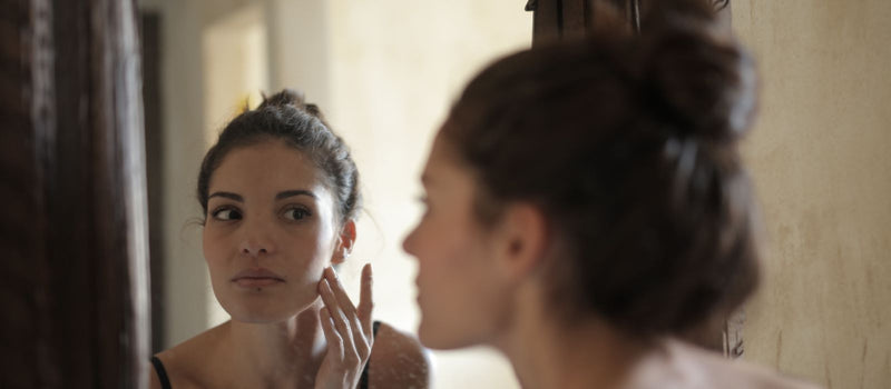Woman checking her skin in the mirror during her skincare routine