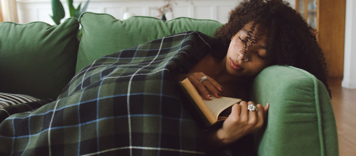Woman relaxing under a blanket on a sofa reading a book in the evening