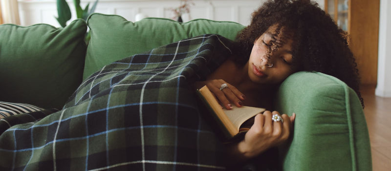 Woman relaxing under a blanket on a sofa reading a book in the evening