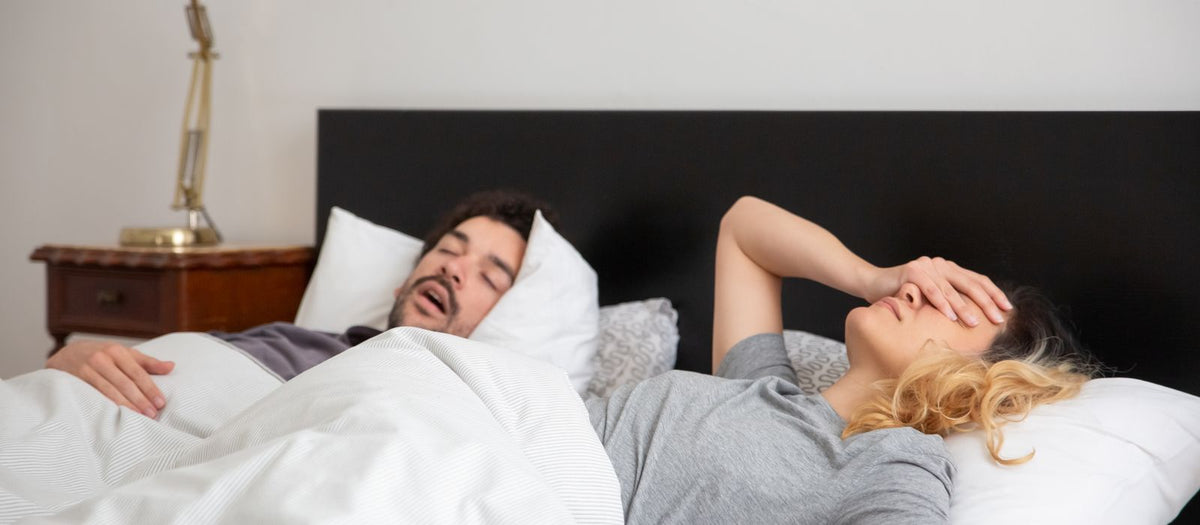 Woman covering her face to block out noise while her partner sleeps