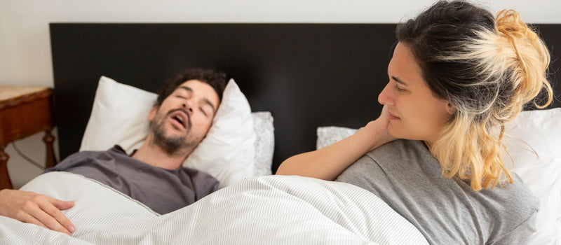 Man snoring in bed next to his restless partner